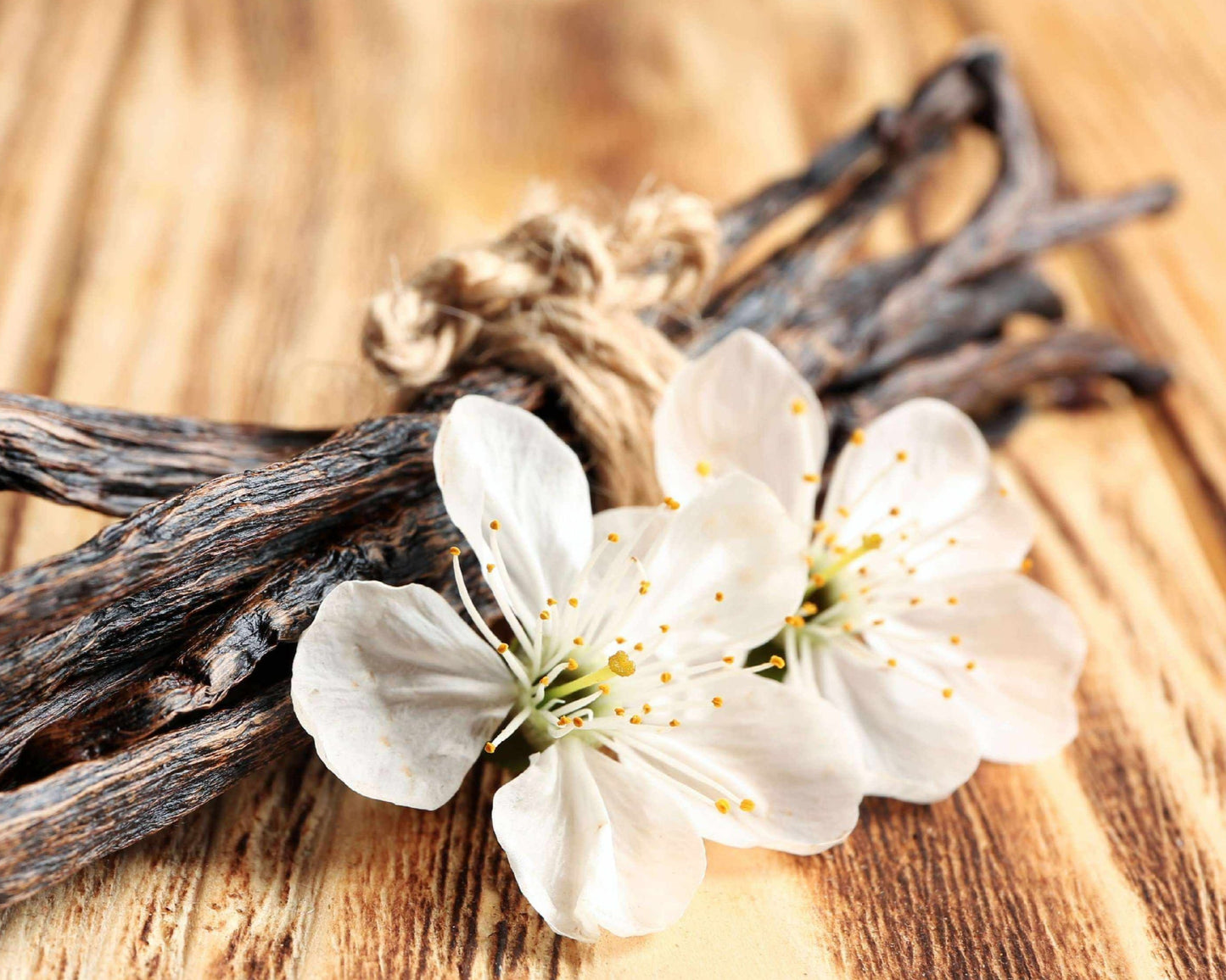 Vanilla pod with white flowers on a wooden surface